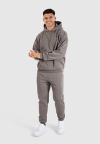Grå hættetrøje og matchende sweatpants lavet af blødt stof, med en afslappet pasform og subtile logo detaljer. Begge dele er ledsaget af hvide sneakers.