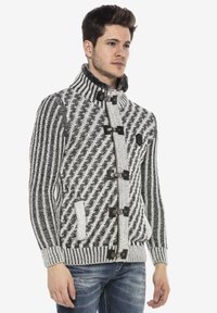 Gebreid sweater in zwart-wit visgraatpatroon, met een hoge kraag, knoopdetails en zijzakken. Gestructureerde afwerking.