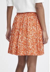 Rok met bloemmotief en elastische tailleband; heeft een oranje en romige print; de stof heeft een gladde textuur en een uitlopende vorm.