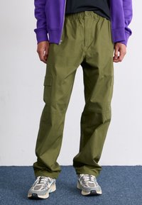 Pantaloni cargo de culoare verde măsliniu cu un talie elastică, două buzunare laterale și o croială lejeră, asortați cu adidași cu model gri și alb.
