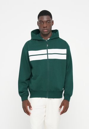 Grøn zip-up hættejakke med en frontlynlås, hvid stribet design over brystet, ribbede manchetter og talje, lavet af blødt, tekstureret stof.