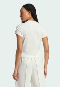 Biała koszulka z krótkim rękawem, uszyta z miękkiej bawełny, o luźnym kroju i okrągłym dekolcie, w zestawieniu z jasnobeżowymi spodniami plisowanymi.