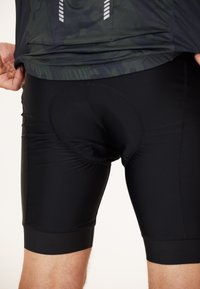 Schwarze Radshorts mit einer gepolsterten Einlage, ausgestattet mit einem enganliegenden Design und glatter Textur. Die Shorts haben eine mittellange Beinlänge und dehnbares Material.