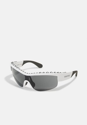 Lunettes de soleil au design épuré, verres teintés noirs, monture blanche ornée de cristaux transparents le long du bord supérieur, et branches flexibles noires.