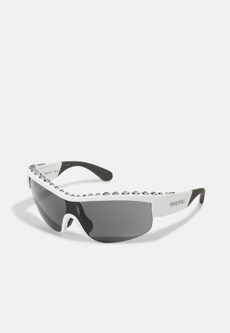 Gafas de sol con un diseño elegante, lentes teñidos de negro, montura blanca adornada con cristales transparentes a lo largo del borde superior y patillas flexibles de color negro.