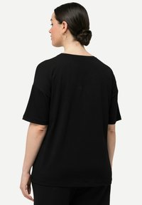Camiseta de algodón negra con un ajuste relajado, mangas cortas y cuello redondeado. Diseño simple sin patrones ni acentos visibles.