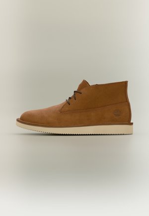 Brauner Wildleder-Stiefelette mit dunklen Schnürsenkeln und weißer Sohle, im Seitenprofil auf neutralem Hintergrund gezeigt.