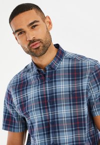 Camisa de botones de cuadros de manga corta en tonos azul, marino y rojo; cuenta con cuello tipo camisa y logo bordado en el pecho.