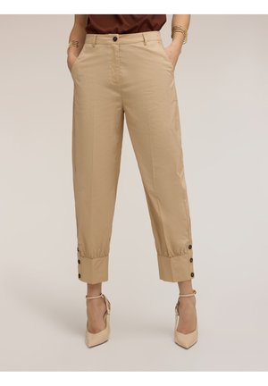 Beige bukser med høj talje og smalle ben med knapper ved manchetterne, sidelommer, båret med beige ankelremshæle og en brun top.