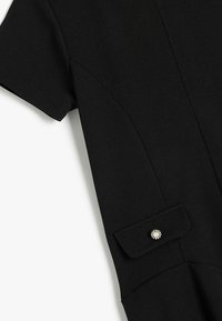Schwarzes Kleid mit kurzen Ärmeln, das ein strukturiertes Design aufweist und einen dekorativen Knopf-Akzent an der Ärmeltasche hat. Glatte Stofftextur.