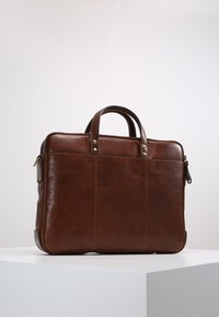 Attaché en cuir marron avec double poignées de transport, coins renforcés et couture visible ; design épuré, texture lisse et sans matériel visible.