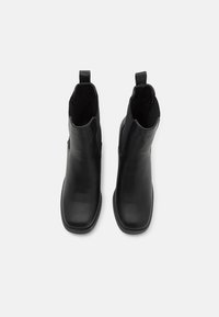Botine din piele neagră până la gleznă, cu o textură netedă, vârf rotund, panouri laterale elastice și bucle pentru o îmbrăcare ușoară.