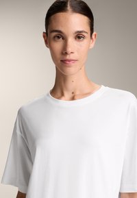 Hvid bomuld T-shirt med en afslappet pasform, rund halsudskæring og korte ærmer, der har en glat tekstur og minimale detaljer.