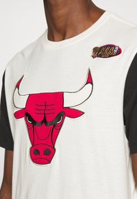 Tričko s krátkým rukávem, na přední straně s velkým červeným bull motivem, vyrobené z bavlny s černými rukávy. Obsahuje vyšitý nášivku "NBA Finals".