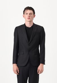 Completo a righe nere con giacca a un bottone e due bottoni, abbinato a una camicia nera. Fit su misura e texture liscia.