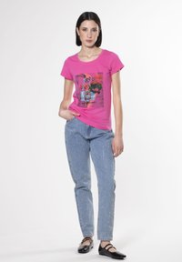 Camiseta de algodón rosa con diseño gráfico floral, combinada con unos jeans de mezclilla azul claro con manchas plateadas y unas bailarinas negras.