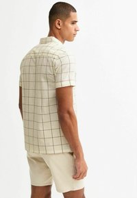 Chemise à manches courtes à boutonner en beige clair avec un motif à carreaux, dotée d'un col, d'un ourlet droit et d'un tissu doux et texturé.