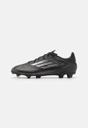 Schwarzer Fußballschuh mit weißem und goldenem Streifendesign, strukturiertem Obermaterial und geformten Stollen auf einfarbig hellem Hintergrund.