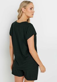 Mono corto de color verde oscuro, con mangas cortas y un corte relajado, que presenta un escote redondo y una tela suave y texturizada, adecuado para uso casual.