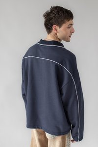 Navy blue oversized sweatshirt with white accent stitching, features a ribbed collar and dropped shoulders, made from a soft textured fabric.