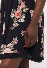 Λουλουδάτο φόρεμα με μαύρο τσαλακωμένο ύφασμα, διακοσμημένο με μεγάλα ροζ και κρεμ λουλούδια. Δαντέλα στο κάτω μέρος, με χαλαρή εφαρμογή και κοντά μανίκια.