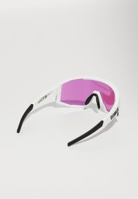 Sportzonnebril met een witte rand, roze lenzen en zwarte accenten. Beschikt over een omsluitend ontwerp en een gestructureerde grip op de armen.