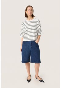 Stribet, løstsiddende hvid- og sort t-shirt parret med mellemlange blå denim shorts. Svarte spidse sko med stropper fuldender looket.
