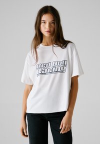 T-shirt en coton blanc avec le logo "Red Bull Racing" en police serif bleue. Manches courtes, encolure ronde, coupe décontractée.