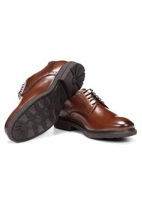 Zapatos de vestir de cuero marrón con detalles de brogue, punta redondeada y suela de goma texturizada. Presentan cierre de cordones y acabado suave.
