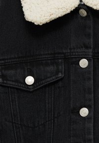 Veste en denim noire avec col sherpa blanc, boutons-pression argentés et poche à rabat sur la partie supérieure de la poitrine.