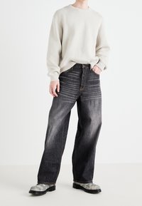 Jeans de mezclilla negros holgados con un acabado desgastado, combinados con un suéter de punto gris claro. El conjunto incluye un par de botas negras texturizadas.