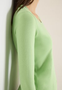 Long-sleeved top in light green, made of soft fabric, featuring a v-neck design and a fitted silhouette, with smooth texture and minimal stitching.