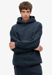 Sudadera azul marino hecha de tela suave, con capucha ajustable, puños acanalados y un pequeño logo en el pecho. Corte holgado.