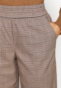 Checkered trousers featuring a woven, textured fabric in shades of brown, black, and red, with an elastic waistband and side pockets.