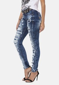 Versleten blauwe denim jeans met gescheurde accenten aan de zijkanten en een getailleerd ontwerp. Gepaard met zwarte hoge hakken sandalen.