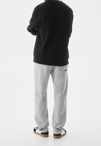 Black sweatshirt with ribbed cuffs, paired with light gray sweatpants. Footwear features a black and white design with a tan sole.