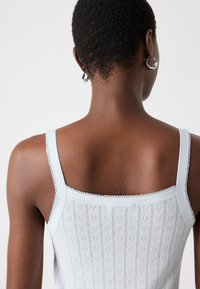 Hellblaues, gestricktes Tanktop mit dünnen Trägern; es hat ein strukturiertes Muster aus kleinen Herzen und gewellten Kanten entlang des Ausschnitts.