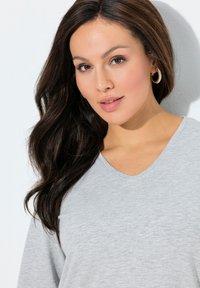 Top grigio con scollo a V in tessuto morbido, caratterizzato da un dettaglio a forma di cuore discreto sul petto. Il design presenta una vestibilità rilassata e una texture liscia.