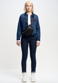 Denim jakna v modri barvi s podrobnostmi na gumbih, v kompletu s oprijetimi temno modrimi džinsom. Črna torbica za čez ramo in bele platforme.