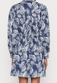 Robe bleu marine avec un imprimé de feuilles blanches, manches longues et taille élastique. Dispose d'un col et de poignets boutonnés, fabriquée à partir d'un tissu léger.
