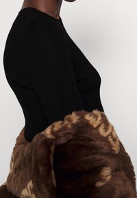 Czarny, prążkowany top z dopasowanym krojem, zestawiony z brązowym, sztucznym futrem z delikatnym wzorem na krawędzi.