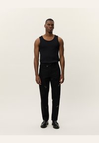 Un top sin mangas negro acanalado combinado con jeans negros rasgados, con parches y un ajuste relajado. Lleva puestas unas botas negras con cordones.