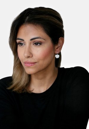 Orecchini a goccia argentati a forma di foglia, indossati da una persona con capelli castani di lunghezza media. Indossano un top nero su uno sfondo bianco.