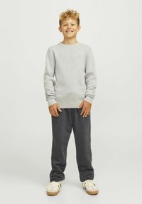 Grå långärmad tröja, mjuk textur, rund halsringning. Mörkgrå joggingsbyxor, lös passform. Ljust färgade skor med beige accenter.