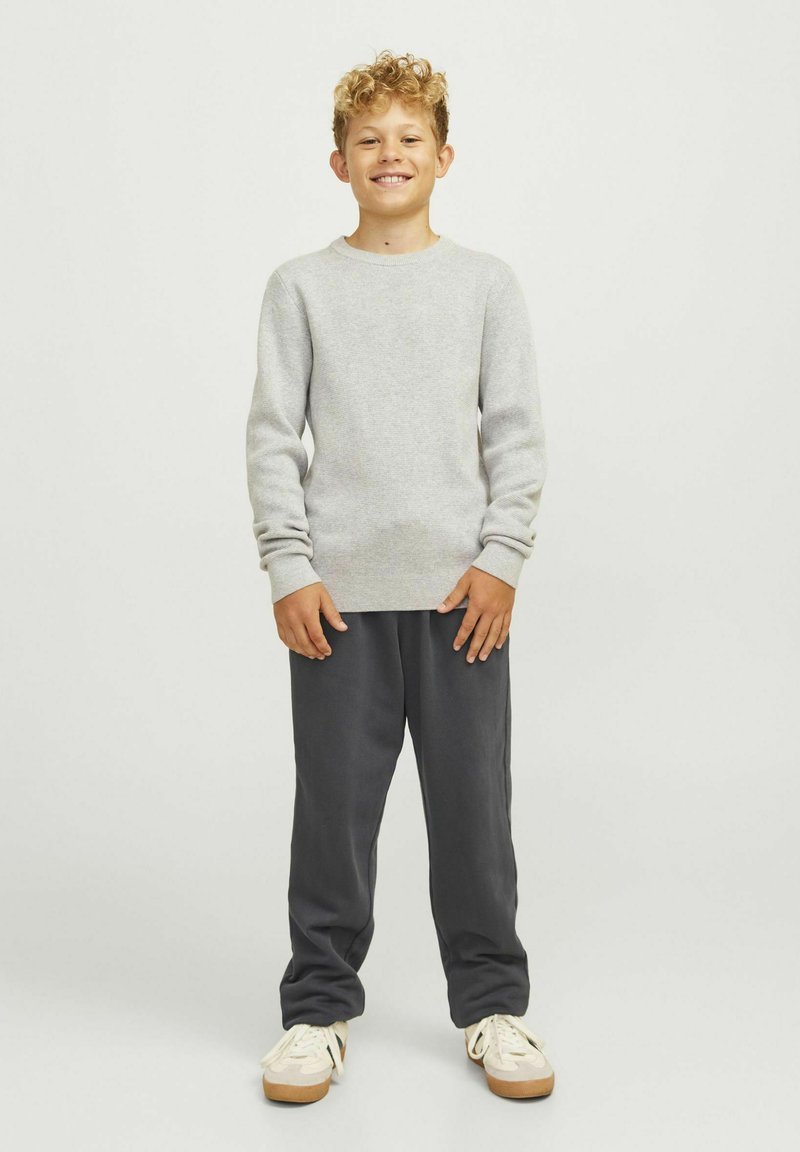 Grå långärmad tröja, mjuk textur, rund halsringning. Mörkgrå joggingsbyxor, lös passform. Ljust färgade skor med beige accenter.