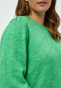 Grüner Strickpullover mit einem strukturierten Muster aus diagonalen Linien und einem runden Ausschnitt. Das Material wirkt weich mit einer leicht samtigen Textur.