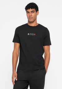 Μαύρο κοντομάνικο μπλουζάκι από βαμβάκι, με κεντρικό λευκό και κόκκινο λογότυπο "TOMMY HILFIGER" στο στήθος. Απλός, στρογγυλός γιακάς.