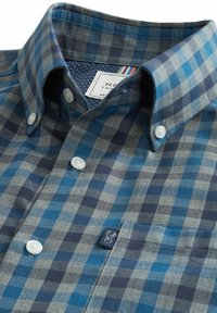 Camisa de cuadros en tonos azul y gris. Presenta un collar puntiagudo, botones blancos y un parche con logo en el bolsillo del pecho. Fabricada en una mezcla de algodón.