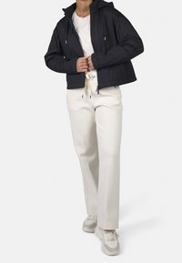 Giacca nera trapuntata con cappuccio, dotata di chiusura con zip e tasche laterali, abbinata a pantaloni crema e sneakers beige. Texture liscia.