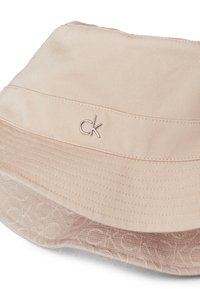 Jasnoróżowa kapelusz typu bucket wykonany z miękkiego materiału, z logo "CK" w kolorze srebrnym oraz teksturowanym paskiem z delikatnym wzorem.